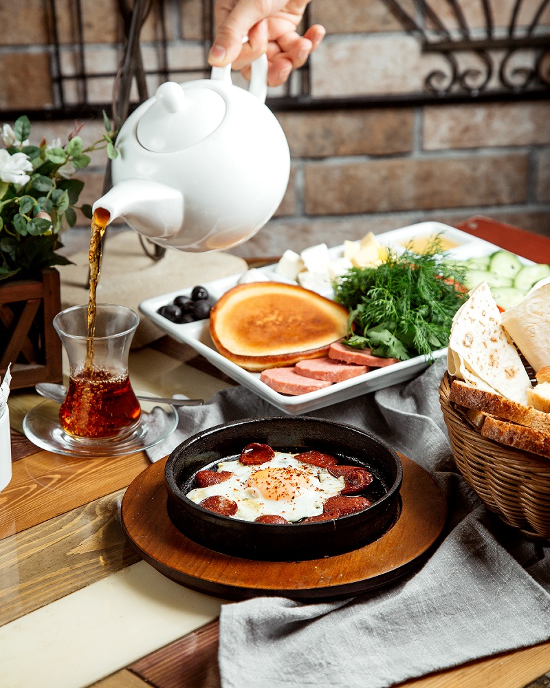 breakfast setup with egg with sausages pancake herbs cheese vegetables and tea
